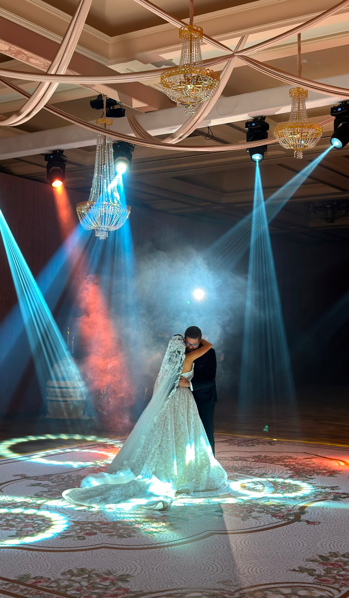 Milad and Reem sharing their first dance under chandeliers and stage lights